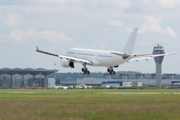 Close up of wide-body modern passenger airplane almost landed at runway, airport and air traffic control on background/ Low over the runway, copy space/ Vacation, aviation, travel, trip - concept/