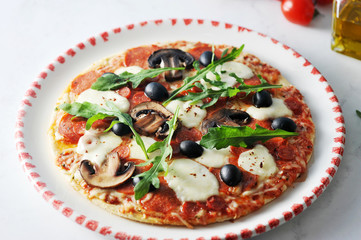 Pizza on the platter. The structure of the filling includes olives, mushrooms, salami, arugula, mozzarella, tomatoes. Close-up. View from above. 