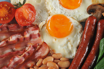 On a plate fried bacon, sausages, frited fresh tomatoes and champignons, white beans in tomato sauce, toast, fried eggs. Close-up. View from above. Macro photography.