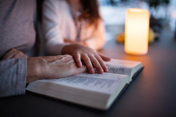 A small girl and grandmother reading bible at home.