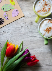 Tulips on wooden with two cups of coffee. Invitation postcard for mother's day or international women's day. Spring paper colorful birds. Handmade origami. Punchy pastels. Cappuccino with cinnamon.
