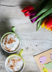 Tulips on wooden with two cups of coffee. Invitation postcard for mother's day or international women's day. Spring paper birds on craft paper envelope. Handmade origami. Punchy pastels. Cappuccino.