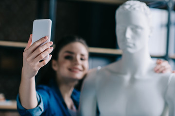 selective focus of smiling woman taking selfie together with mannequin, perfect relationship dream concept