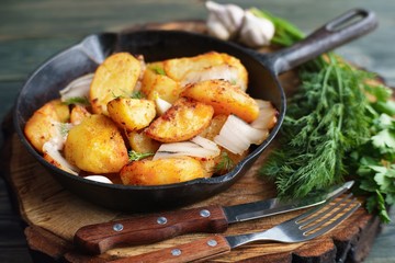 Appetizing hot roasted potatoes with bacon  served with cutlery and greenery on cast iron frying pan, Ukrainian cuisine, countryside still life, homemade traditional meals concept