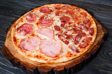 Appetizing pizza with bacon, salami,ham and pepperoni served on chopped wood, close up. Italian food, restaurant menu