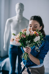 selective focus of young woman with bouquet of flowers and mannequin behind, one way love concept