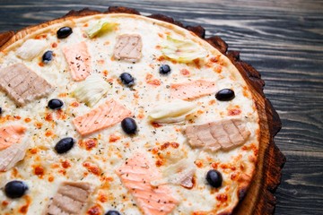 Appetizing pizza with salmon, tuna and olives on wood, close up. Italian food, kitchen background