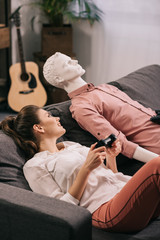 woman with manikin near by playing video game at home, loneliness concept