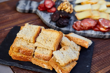 Fried crusty bread on a background of a set of various cheeses, smoked sausage, apricot orange sauce, walnuts, blood sausage and on a marble board and a wooden table.