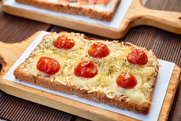 A set of sandwiches with melted cheese and sun dried tomatoes and baked cheese and salmon on a light cutting board and a brown wooden table. Photographed with natural light.