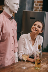 smiling woman looking at mannequin at table with wineglasses at home, perfect relationship dream concept