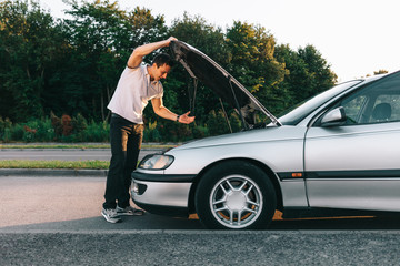 Young attractive caucasian man in white t-shirt standing by the broken car