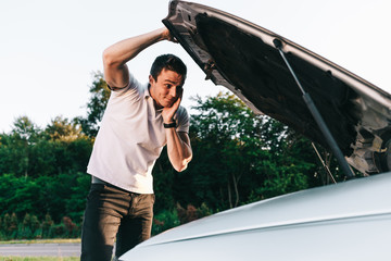 Young attractive caucasian man in white t-shirt standing by the broken car