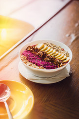 Superfood tropical smoothie bowl with dragon fruits, banana, granola on a wooden coffee table. Morning sunlight. Minimalism food photography concept. Copyspace