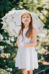 Outdoor portrait of romantic little girl, wearing white dress, gloves, flower headband, holding lace umbrella