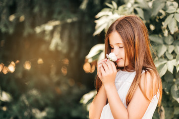 Outdoor portrait of adorable little girl with white rose flower
