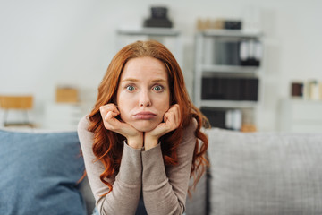 Young upset woman sitting on sofa at home