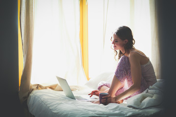 Young beautiful woman sitting in bed with laptop.