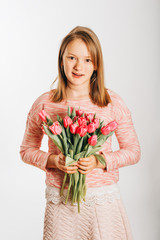 Studio image of cute preteen girl wearing sweatshirt, holding pink tulips