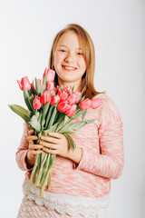 Studio image of cute preteen girl wearing sweatshirt, holding pink tulips