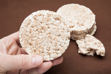 A hand holds a dietary rice snack on a brown background.