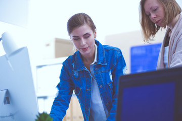 Two young woman standing near desk with instruments, plan and laptop.