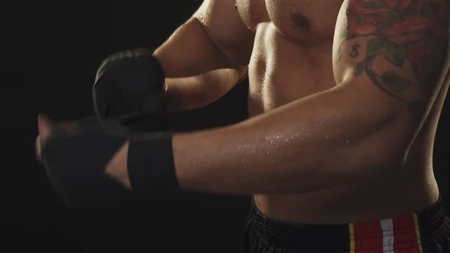 Ripped male boxer with sweaty torso taking off hand wraps after fighting