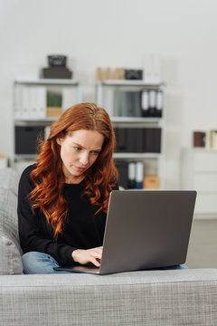 Pretty young redhead woman using a laptop at home