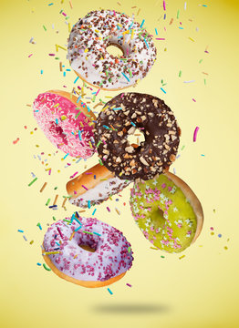 Tasty doughnuts in motion falling on pastel yellow background.