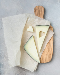 Wooden board with tasty goat cheese on concrete stone background. Cheese heart. Romantic holiday table setting. Beautiful background with blank. Restaurant concept.