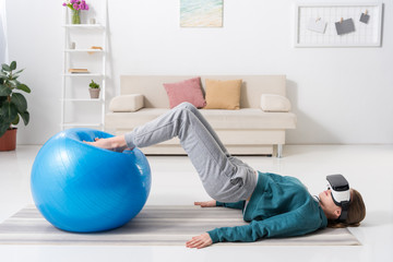 side view of girl exercising with fitness ball and in virtual reality headset at home