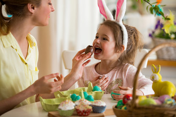 Mother and daughter celebrating Easter, eating chocolate eggs. Happy family holiday. Cute little...