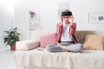 girl sitting in lotus position with virtual reality headset on sofa at home