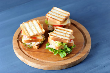 On a wooden tray are three mini sandwiches made from roasted white bread. The filling of the...