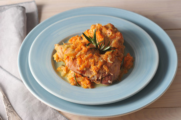 Rabbit is cooked with rosemary and carrots. The dish is decorated with a branch of rosemary. In the frame cutlery and napkin. Light wooden background. Close-up. Macro photography.