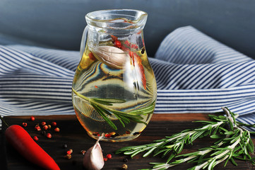 Jug with olive oil. In the oil added rosemary, bell pepper, garlic. Next to the jug, a cloth napkin...
