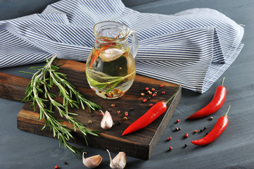 Jug with olive oil. In the oil added rosemary, bell pepper, garlic. Next to the jug, a cloth napkin...