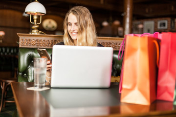 Happy student sits with laptop and shopping bags in a cafe and calls a friend