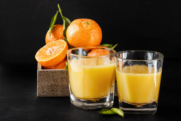 Ripe tangerines with leaves and juice glass on dark background
