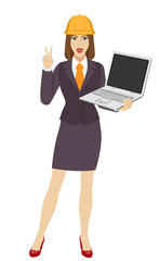 Businesswoman in construction helmet holding a laptop notebook and showing victory sign