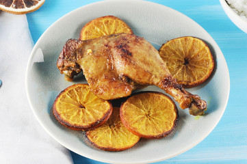 Duck thigh baked with oranges. A classic way to make ducks. A fragrant and delicious dish on a light plate. In the picture, a napkin.  Blue background. Close-up.