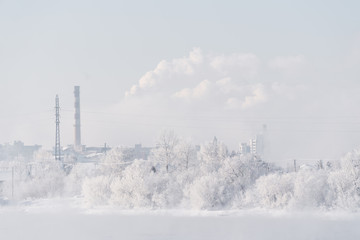 Snow covered on trees with industrial factory and smoke on the sky, white forest landscape