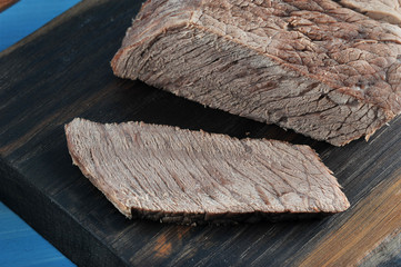 A piece of boiled beef on a wooden board. One slice is cut from the piece. On the cut, the fibrous structure of the meat is clearly visible. A close-up. Macro photography.