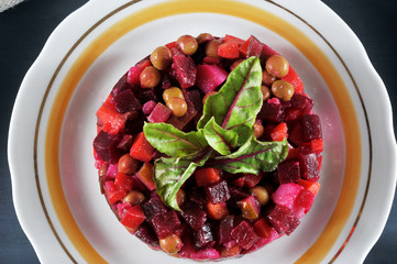 A portion of Russian salad is a vinaigrette. In the composition boiled beets, potatoes, carrots, green peas, salted cucumber. Dark background. View from above. Close-up. Macro photography.