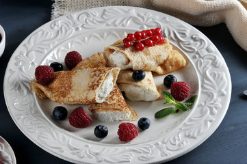 Pancakes stuffed with cottage cheese. The dish is decorated with berries of raspberries, blueberries and red currants. Dark wooden background. Close-up. Macro photography.