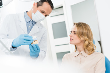 Fototapeta premium Doctor showing jaws model to female patient in modern dental clinic