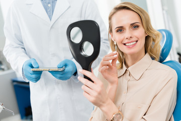 Female patient choosing tooth implant looking at mirror in modern dental clinic