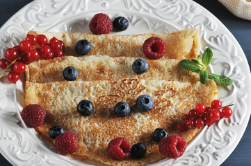 Plate with large pancakes. Pancakes are decorated with berries of red currants, raspberries, blueberries. Close-up. View from above. Macro photography.