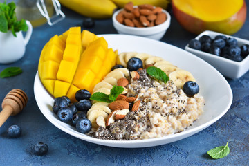 Good morning! Breakfast with oatmeal, banana, mango, blueberries and chia seeds on a concrete background.