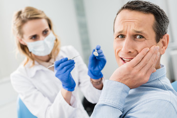 Female dentist checking patient teeth with mirror in modern dental clinic